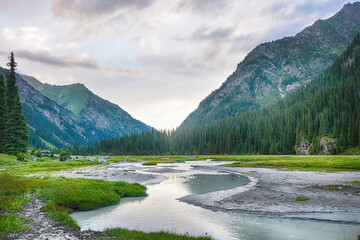 Idyllic summer landscape with hiking trail in the mountains with beautiful fresh green mountain pastures, river with reflection and forest.