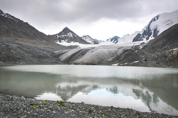 Idyllic winter landscape with hiking trail in the mountains. Rocks, snow, lake, glacier and stones.