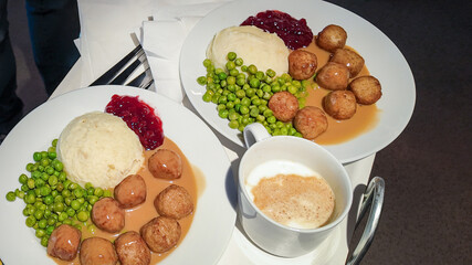 Two plates of Swedish meatballs with mashed potatoes, peas, and lingonberry sauce exemplify traditional Scandinavian cuisine, ideal for celebrating Midsummer