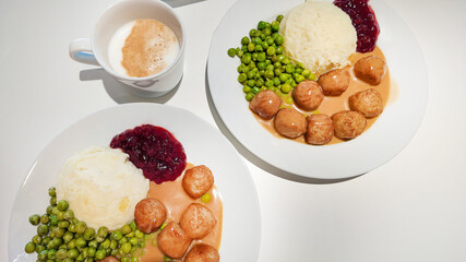 Two plates of traditional Swedish meatballs with mashed potatoes, peas, and lingonberry sauce, perfect for celebrating Midsummer