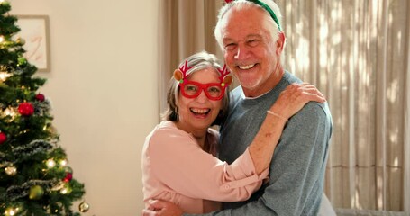 Senior couple wearing festive accessories smiling joyfully by Christmas tree at home - Powered by Adobe