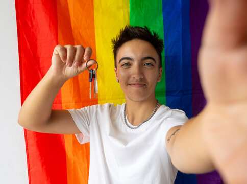 Proud trans man with new home keys against a pride flag