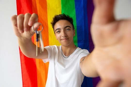 Trans man holding keys in front of a pride flag