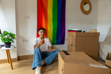 Trans man relaxing in new home with pride flag backdrop