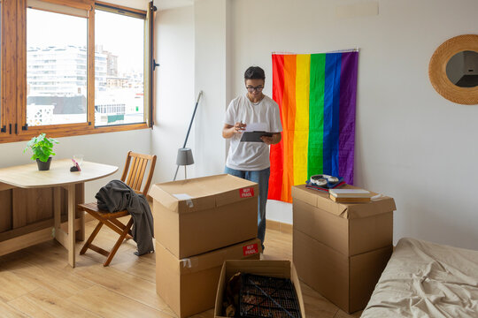 Trans man organizing new home beside pride flag
