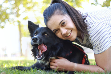 Young woman lying on the grass hugging her Border Collie dog, sharing a joyful and affectionate moment