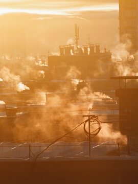 A chilly winter morning dawns, with the sun rising over the rooftops of tall buildings in Russia. The warm air rises from the vents of central heating systems