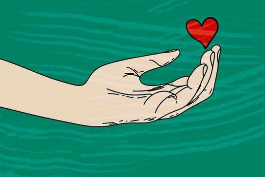 Hand gently holding a red heart on a green background