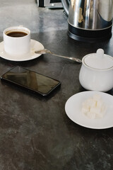  A phone rests on the kitchen table next to a cup of coffee. A cozy scene that reflects everyday moments and the enjoyment of coffee in a home setting.