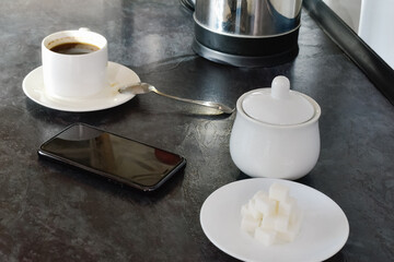  A phone rests on the kitchen table next to a cup of coffee. A cozy scene that reflects everyday moments and the enjoyment of coffee in a home setting.