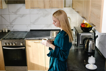  A young woman enjoys fresh aromatic coffee in her cozy kitchen. The concept of a morning ritual that awakens the senses and creates an atmosphere of comfort and inspiration for the day ahead.