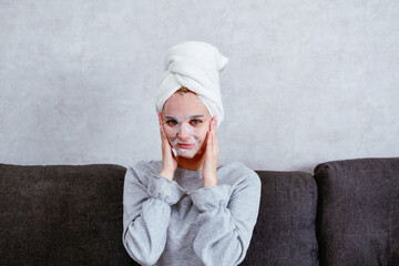 A young woman wearing a facial mask sits at home, immersed in a spa-like atmosphere. A cozy moment of self-care that emphasizes the importance of relaxation and skincare.
