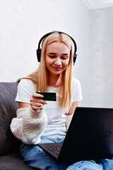 Naklejka premium A young woman holding a credit card uses her laptop to work from home. A moment of online shopping and internet banking, showcasing the convenience and opportunities of modern business.