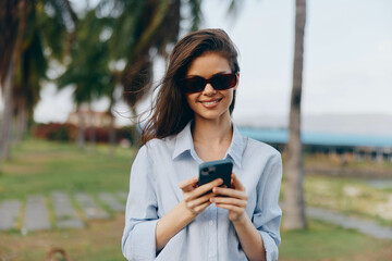 Woman, sunglasses, palm tree, cell phone, smile a woman in sunglasses holds a cell phone and smiles while standing in front of a palm tree, capturing a moment of tropical relaxation