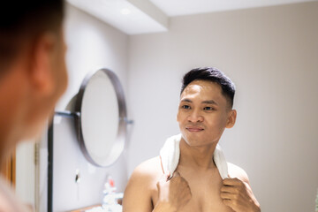 A confident man stands in front of a bathroom mirror, draped with a towel, reflecting positive...