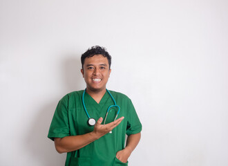 Asian male doctor in green suit with stethoscope around his neck, pointing and giving presentation with enthusiastic expression. Plain background highlights the doctor's inviting attitude.