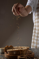 A hand sprinkles seeds over thick slices of freshly baked artisan bread, creating a rustic and appetizing culinary scene on a wooden surface with warm lighting.