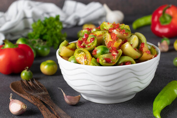 Salad of green tomatoes with hot peppers and garlic in white salad bowl