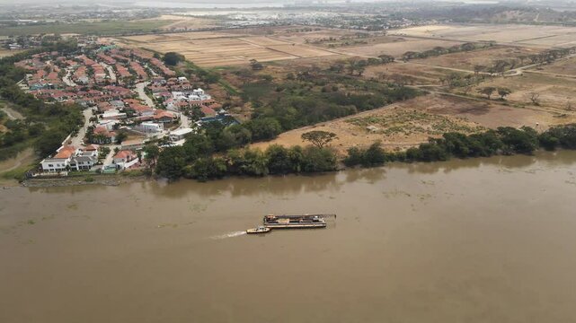 Tugboat pushes a massive crane down Ecuador&rsquo;s Daule River, showcasing industrial power in a tropical setting. Ideal for logistics, machinery, and South American waterways projects.