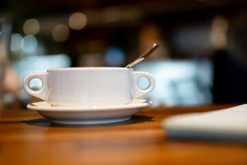 A warm, inviting coffee cup with spoon on a wooden table in a quiet cafe, capturing a cozy, calm atmosphere with soft background blur.