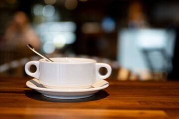 A warm, inviting coffee cup with spoon on a wooden table in a quiet cafe, capturing a cozy, calm atmosphere with soft background blur.