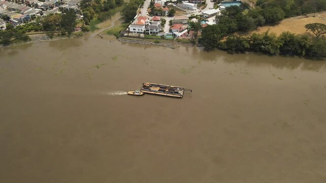 Tugboat pushes a massive crane down Ecuador&rsquo;s Daule River, showcasing industrial power in a tropical setting. Ideal for logistics, machinery, and South American waterways projects.