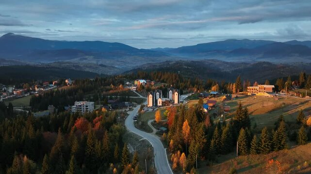 The first light of sunrise spills over the Carpathian region, bathing the landscape in a delicate, golden hue. The hotel hub nestles quietly in the early morning calm. October, 2024.