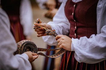 Close-up of hands holding and tying traditional woven Latvian belts with intricate patterns, showcasing cultural craftsmanship and folk attire..