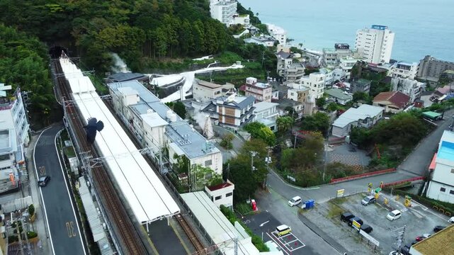 Captured on a cloudy day, this scenic view highlights the local train tracks running through mountain countryside, with surrounding fields and traditional houses adding charm to the tranquil atmospher