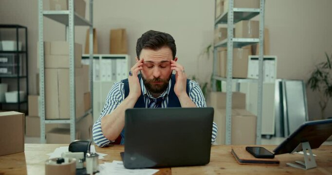 Tired man, laptop or logistics with headache for stress, anxiety or mistake at warehouse. Frustrated businessman, employee or distributor with migraine, vertigo or depression for debt or supply chain