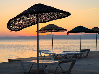 Sunrise over calm waters with beach umbrellas arranged neatly along the shore at a serene coastal location