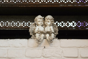 Two little stone angels sit on a brick wall and read a book