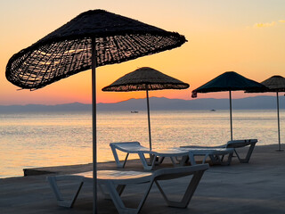Sunrise over calm waters with beach umbrellas arranged neatly along the shore at a serene coastal location