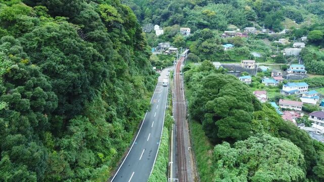 Captured on a cloudy day, this scenic view highlights the local train tracks running through mountain countryside, with surrounding fields and traditional houses adding charm to the tranquil atmospher
