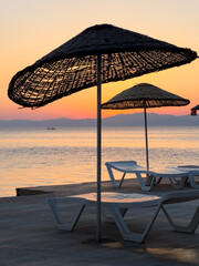 Sunrise over calm waters with beach umbrellas arranged neatly along the shore at a serene coastal location