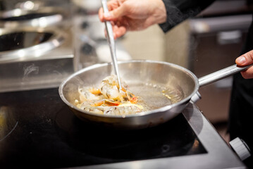 Close-up of a chef cooking shrimp in a stainless steel pan over a stove, capturing the sizzle and culinary skill. Perfect for culinary, cooking, and food preparation themes.