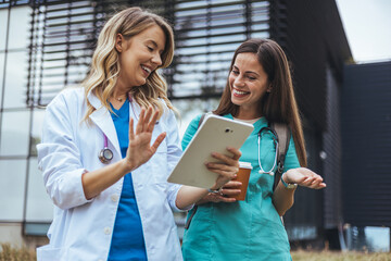 Obraz premium Two Female Healthcare Professionals Discussing Digital Tablet Outdoors