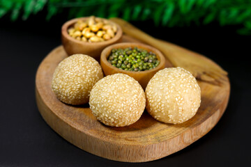Onde-onde, a traditional snack from Indonesia, filled with green beans with chewy sticky rice skin and sprinkled with sesame seeds, placed on a wooden tray that looks very natural