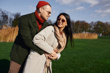 Two individuals share a warm embrace, dressed in stylish autumn clothing, amidst natural beauty.