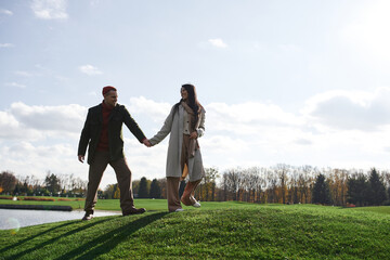 A couple in cozy autumn attire walks hand in hand, basking in the warmth of the sunlit day.