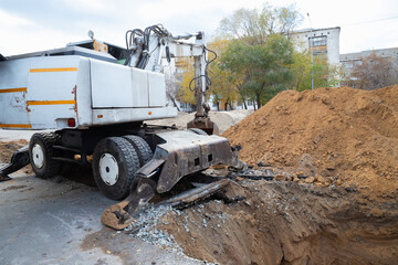 Excavator with bucket. heavy machinery vehicle is actively digging a trench in an urban area, surrounded by piles of dirt and autumn trees, indicating ongoing construction work