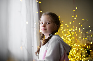 Girl Looking Out the Window with Festive Garland Lights in Background