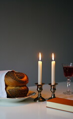 vertical photo Shabbat or Sabbath kiddush ceremony composition with a traditional sweet fresh loaf of challah bread, glass of red kosher wine and candles on a vintage wood table with copy space