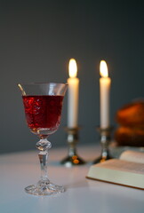 vertical photo Shabbat or Sabbath kiddush ceremony composition with a traditional sweet fresh loaf of challah bread, glass of red kosher wine and candles on a vintage wood table with copy space