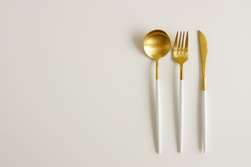 Modern cutlery set gold white colors on light beige background top view with copy space. Elegant...