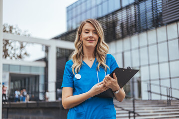 Confident Nurse Standing In Front Of Modern Hospital Building