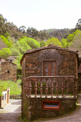 Old stone house with small balcony surrounded by bright green trees. The rustic building sits peacefully in a quiet village, capturing the calm and beauty of the spring season. Remote village setting.