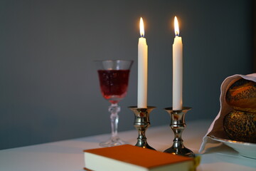 Shabbat or Sabbath kiddush ceremony composition with a traditional sweet fresh loaf of challah bread, glass of red kosher wine and candles on a vintage wood table with copy space