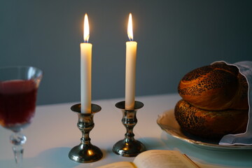 Shabbat or Sabbath kiddush ceremony composition with a traditional sweet fresh loaf of challah bread, glass of red kosher wine and candles on a vintage wood table with copy space
