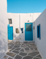 A narrow alleyway in the Cyclades showcases traditional whitewashed houses with bright blue doors. Clothes hang out to dry, adding character to the picturesque setting.